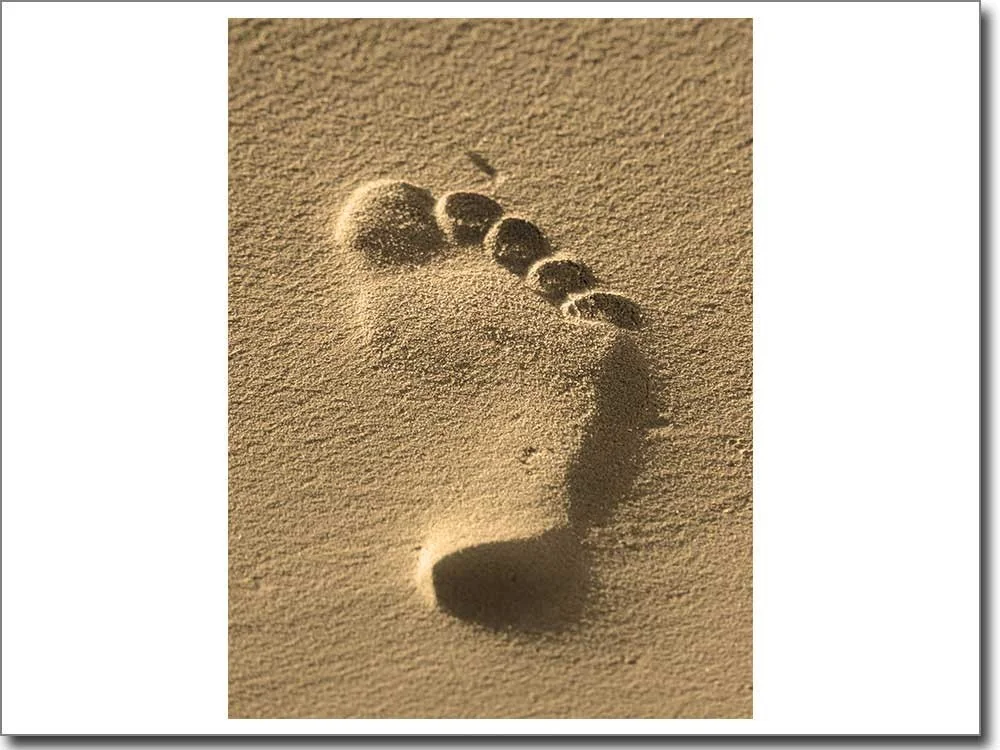 Glasdruck mit Fuß Abdruck im Sand in sepia